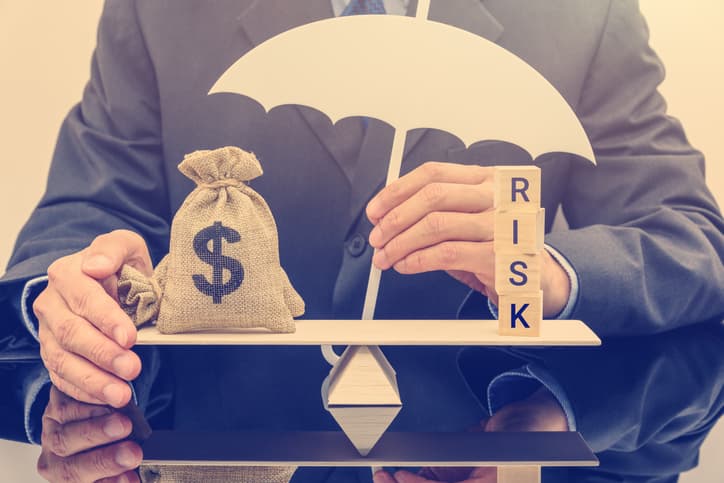 Businessman holding a white umbrella, protecting a dollar bag on basic balance scale, and defending money from being cheat or fraud.