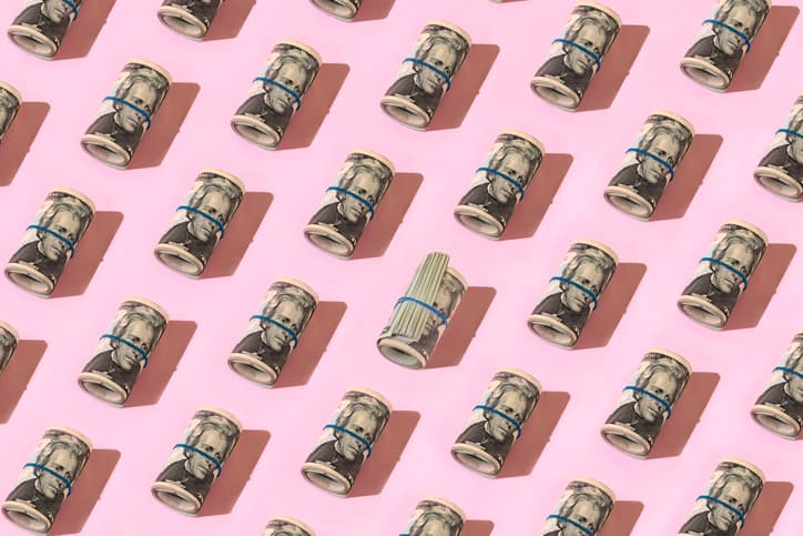 Rolls of dollar bills against a pink background