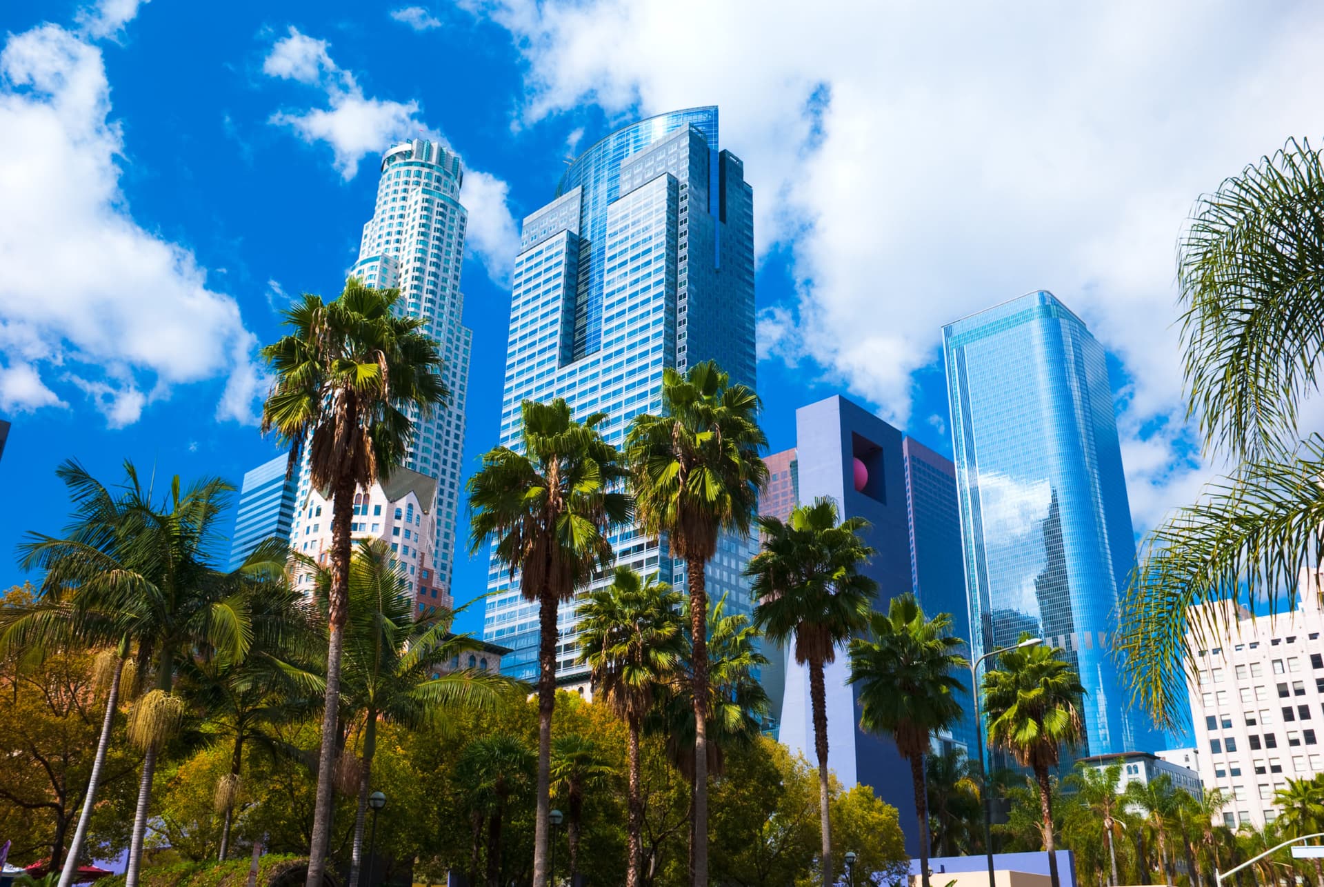 Los Angeles downtown skyscrapers with palm trees and Pershing Square in the foreground with clouds and a blue sky in the background