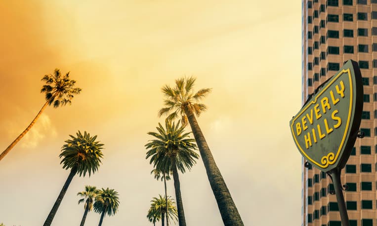 A Beverly Hills street sign backdropped by golden light and palm trees.