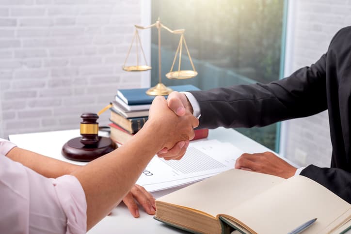 Image of business partners shaking hands with a legal scale in the background.