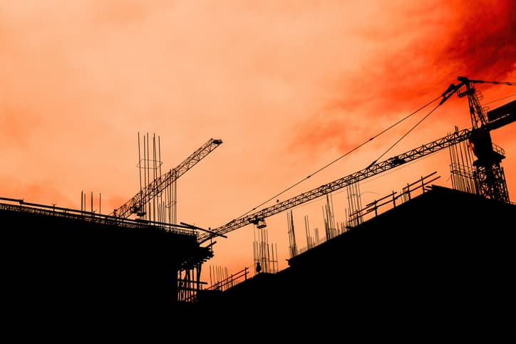 Residential building development and construction, back lit cranes and scaffold with orange sky