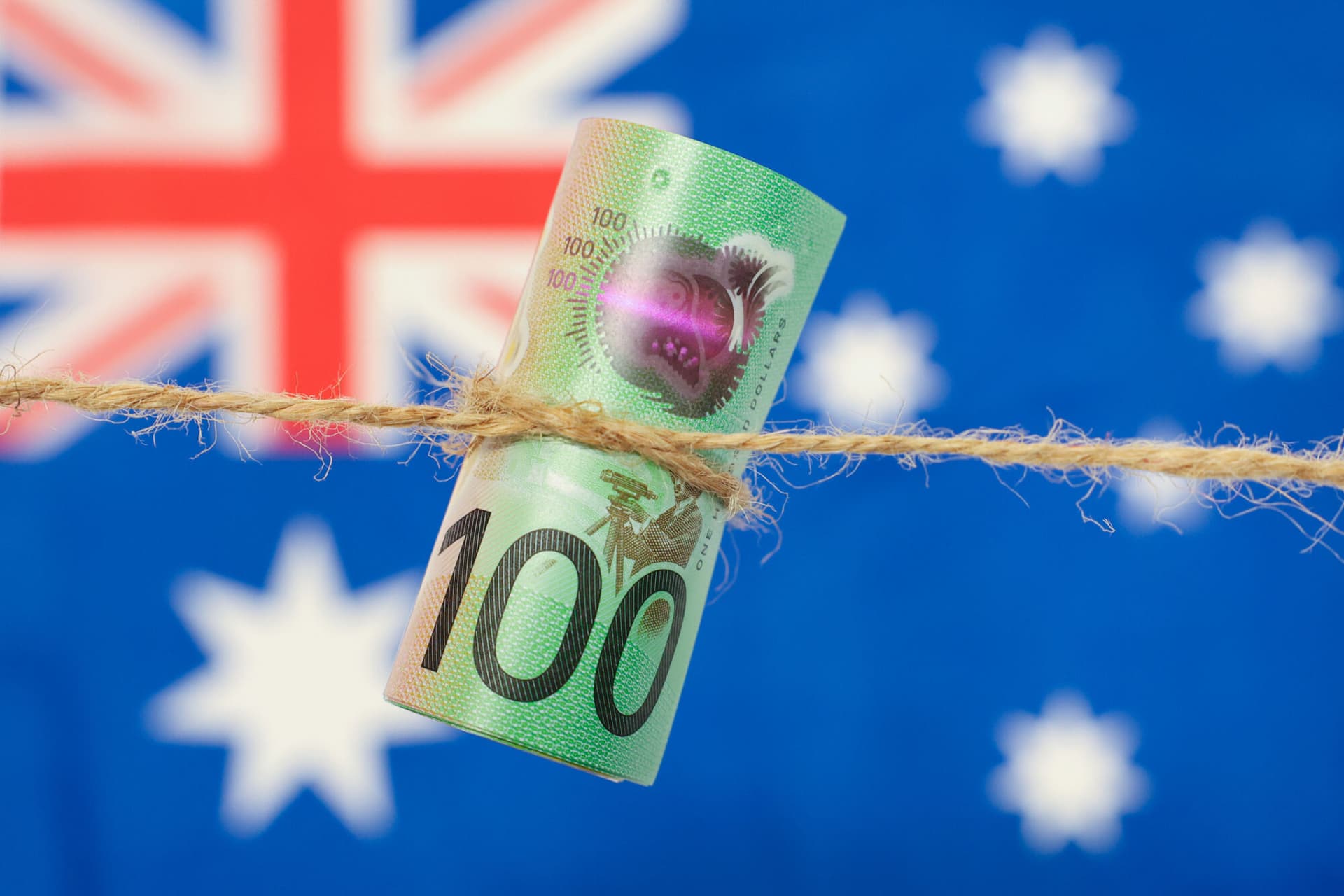 Close up of an Australian one hundred dollar bill tied in string. Australian flag in background.