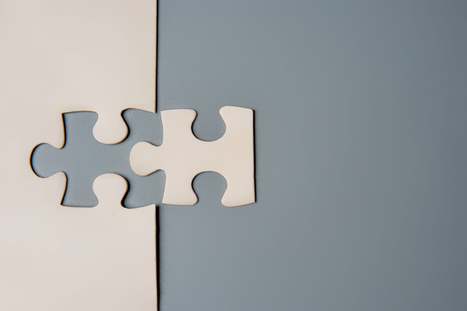 Two puzzle pieces connecting, one white and one grey, on a contrasting background