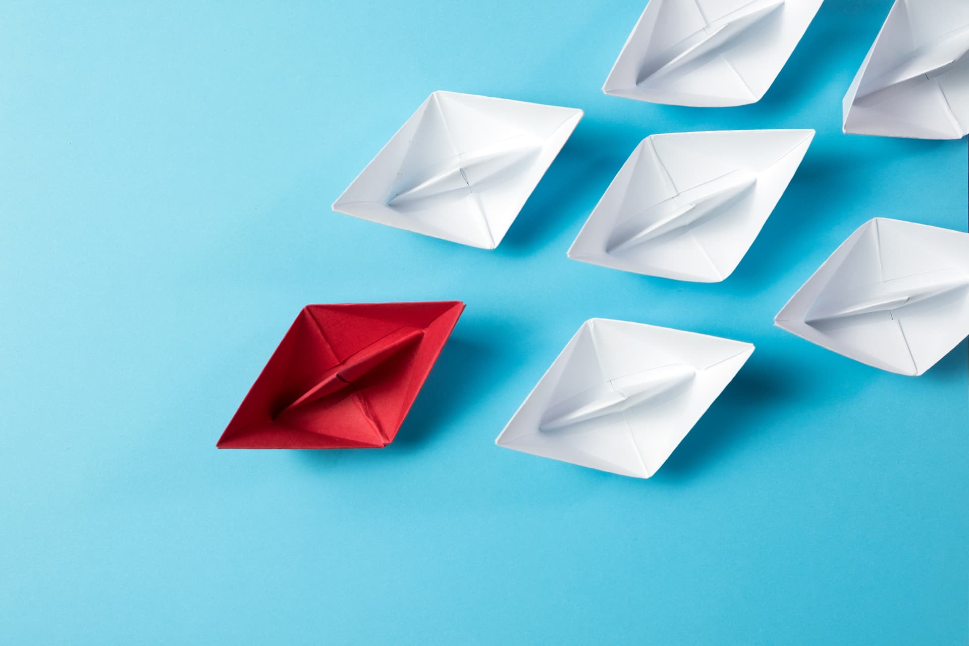 Leadership concept with a red paper ship leading among white ships on blue background